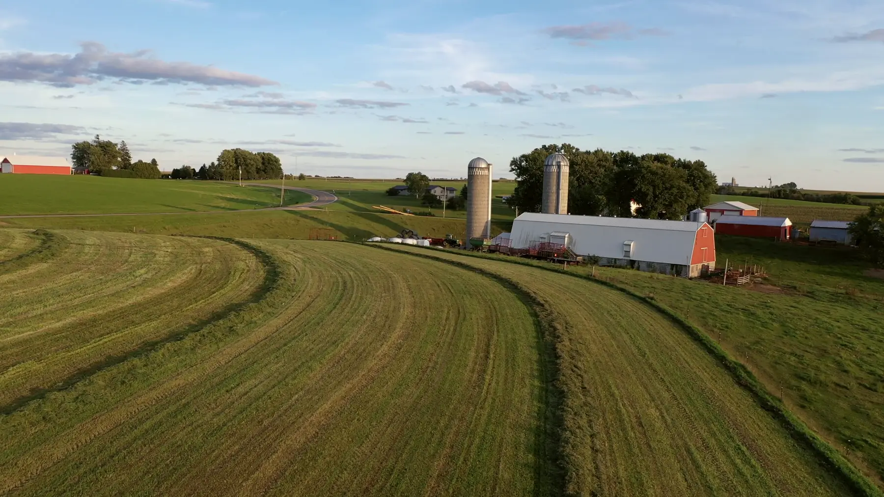 Rolling farmland at golden hour with silos and a red barn